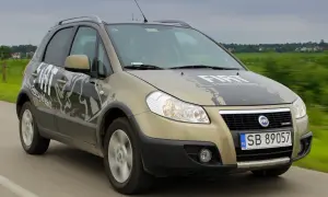 Złoty Fiat Sedici z napisem "FreestyleTeam" na masce i drzwiach jedzie po drodze.