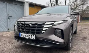Szary Hyundai Tucson Hybrid z charakterystycznym grillem i światłami LED stoi przed garażami.