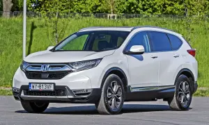 Biała Honda CR-V zaparkowana na zewnątrz, z zielenią w tle.