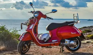 Czerwona Vespa na tle morza. Czy na skuter trzeba mieć prawo jazdy? Kask leży obok.