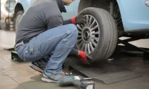 Mężczyzna w czerwonych rękawiczkach zdejmuje oponę z felgi samochodu.