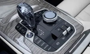 Kryształowa dźwignia zmiany biegów i pokrętło iDrive w BMW X7 2024, otoczone drewnianymi wstawkami i przyciskami trybów jazdy.