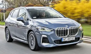 Szary BMW 2 Active Tourer jedzie po drodze, za nim widać żółte krzewy.