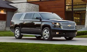 Czarny Chevrolet Suburban na podjeździe przed nowoczesnym, podmiejskim domem z kamiennymi i drewnianymi elementami.