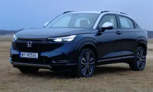 Ciemnogranatowa honda hybryda z srebrnym dachem i lusterkami, zaparkowana na trawiastym polu.