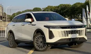 Biały OMODA 9 Super Hybrid z czerwonym wnętrzem stoi na drodze, z drzewami i budynkami w tle.