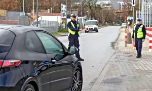 Policjant zatrzymuje czarne auto, być może kolejny raz, by wystawić mandat. W tle biały van i inni funkcjonariusze.