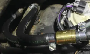 Złoty zawór zwrotny paliwa zamontowany na czarnym wężu paliwowym z oznaczeniem "FUEL INJECTION".
