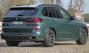 Zielony x5 BMW z napisem XDrive 50e na klapie bagażnika, zaparkowany na bruku.