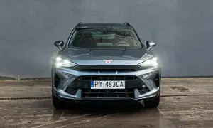 Szary Formentor Cupra z włączonymi światłami, zaparkowany przed betonową ścianą.
