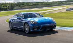 Niebieski Porsche Panamera GTS pokonuje zakręt na torze wyścigowym, z zielonymi wzgórzami w tle.