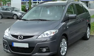 Szary Mazda Premacy stoi na parkingu. W tle widać inne samochody i budynki.