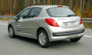 Srebrny Peugeot 207 1.4 benzyna w ruchu drogowym, z naklejkami "Wypróbuj Peugeot" i danymi oddziału.