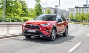 Czerwony Toyota RAV4 2024 na zakręcie drogi, z kierowcą za kierownicą.