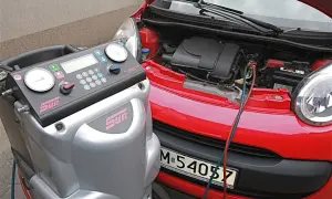 Urządzenie do serwisu klimatyzacji podłączone do czerwonego samochodu. Dowiedz się, ile kosztuje nabicie klimatyzacji.