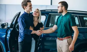 Para młoda uśmiecha się, ściskając dłoń sprzedawcy przy nowym aucie. To ich wymarzony auto w leasing dla osoby prywatnej.