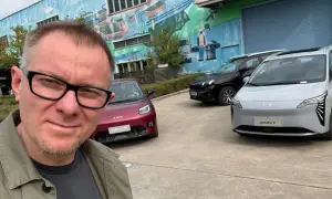 Mężczyzna w okularach pozuje do selfie na tle trzech samochodów marki AION.