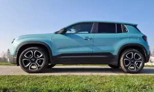 Turkusowy Jeep Avenger, marka samochodu na wprost, stoi na tle błękitnego nieba i zielonej trawy.