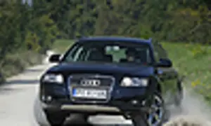 Ciemny Audi allroad pokonuje piaszczystą drogę, wzbijając kurz.