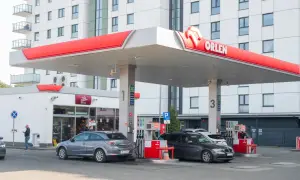 Stacja Orlen z dystrybutorami paliwa. W tle nowoczesny budynek mieszkalny. Ceny paliw, w tym akcyza, wpływają na koszty tankowania.