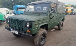 Zielony, wojskowy tarpan honker z plandeką, gotowy do akcji. W tle ciężarówki.