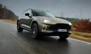 Elegancki Aston Martin SUV przemierza mokrą drogę wśród jesiennych drzew.