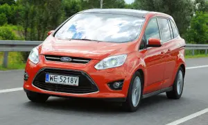 Pomarańczowy Ford C-Max 1.6 benzyna jedzie po drodze, odbijając chmury w szybie.