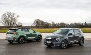 Dwa nowoczesne crossovery Kia Sportage, zielony i grafitowy, stoją na mokrej drodze na tle jesiennego krajobrazu.