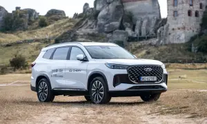 Biały Chery Tiggo 8 Plug-in Hybrid z zasięgiem do 1100 km, zaparkowany na tle ruin zamku. Sprawdź jego cenę!