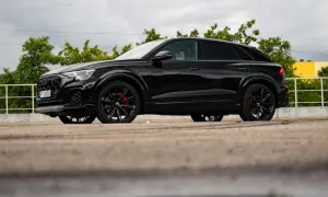 Czarny Audi Q9 z czerwonymi zaciskami hamulcowymi, odbijający się w kałuży. Sprawdź audi q9 cena!
