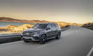Szary Mercedes GLS 580 sunie po krętej drodze nad brzegiem morza podczas zachodu słońca.