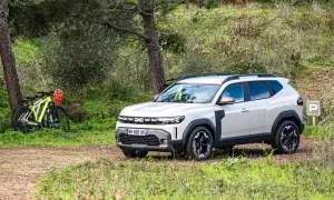 Biały Dacia Duster 1.6 benzyna zaparkowany na leśnej polanie obok rowerów.