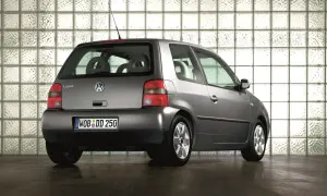 Szary Volkswagen Lupo stoi na ciemnej podłodze, na tle ściany z białych pustaków szklanych.