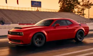 Czerwony Dodge Demon pędzi po torze wyścigowym podczas zachodu słońca, z trybunami w tle.