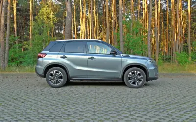 Szary Suzuki Vitara Hybrid zaparkowany na tle sosnowego lasu.