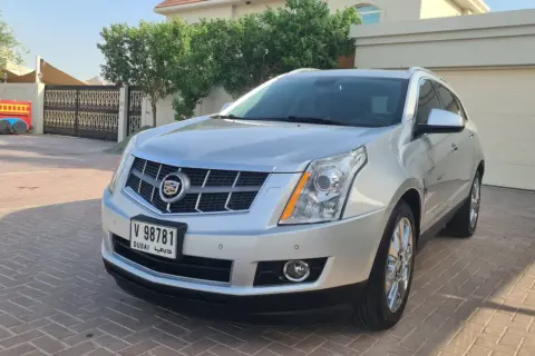 Srebrny Cadillac SRX z Dubai stoi na podjeździe przed domem. Obok widać bramę i fragment czerwonej zabawki.