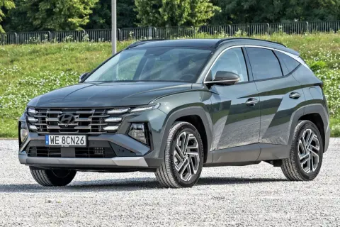 Nowy, tani SUV Hyundai Tucson w ciemnozielonym kolorze, zaparkowany na żwirowej drodze.
