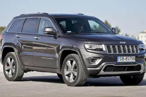 Ciemnoszary Jeep Grand Cherokee 3.6 z polskimi tablicami SB 8575N zaparkowany na zewnątrz.