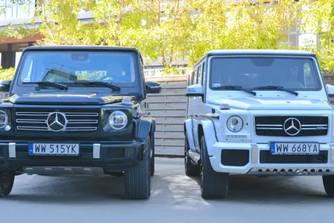 Dwa luksusowe Mercedesy klasy G, czyli gelendy, stoją obok siebie. Jedna jest ciemnozielona, druga biała.