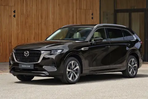 Elegancka, czarna Mazda CX-80 SUV stoi przed nowoczesnym budynkiem z drewnianą elewacją.