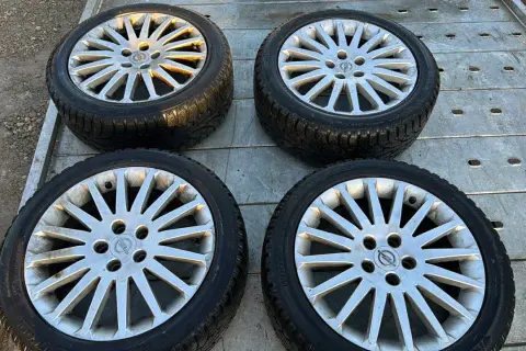 Cztery aluminiowe felgi z oponami zimowymi, z logo Opla, leżące na metalowej platformie.