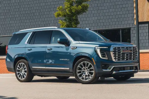 Niebieski GMC Yukon XL Denali lśni na tle nowoczesnej architektury.