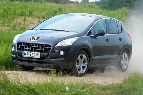 Ciemnoszary Peugeot 3008 2010 na drodze gruntowej, wzbijający tumany kurzu.