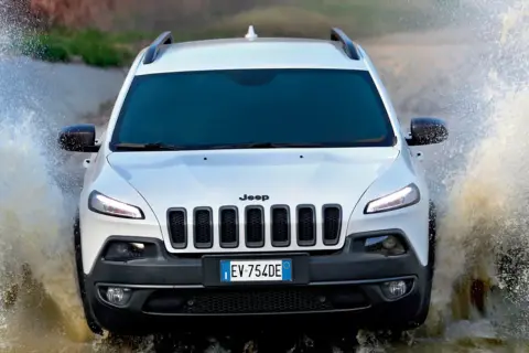 Biały Jeep Cherokee Trailhawk z impetem wjeżdża w wodę, tworząc efektowne rozbryzgi.