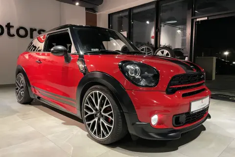 Czerwony mini paceman z czarnymi pasami i felgami stoi w salonie.