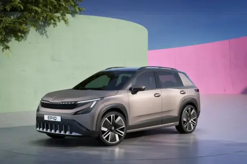 Nowy, elektryczny SUV Škoda Enyaq, z nowoczesnym designem i napisem Enyaq na grillu, prezentuje się na tle kolorowych ścian.