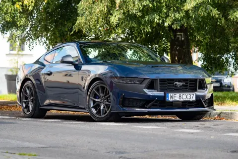 Nowy Ford Mustang 2025 w ciemnoniebieskim kolorze, zaparkowany pod drzewem.