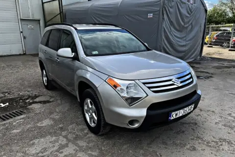 Srebrny Suzuki XL7 zaparkowany przed szarym namiotem.