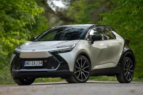 Nowy Toyota C-HR 2024 w kolorze srebrnym z czarnym dachem, zaparkowany na leśnej drodze.