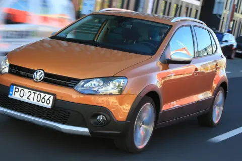 Pomarańczowy Volkswagen Polo Cross w ruchu miejskim, z widocznym kierowcą i innymi samochodami w tle.